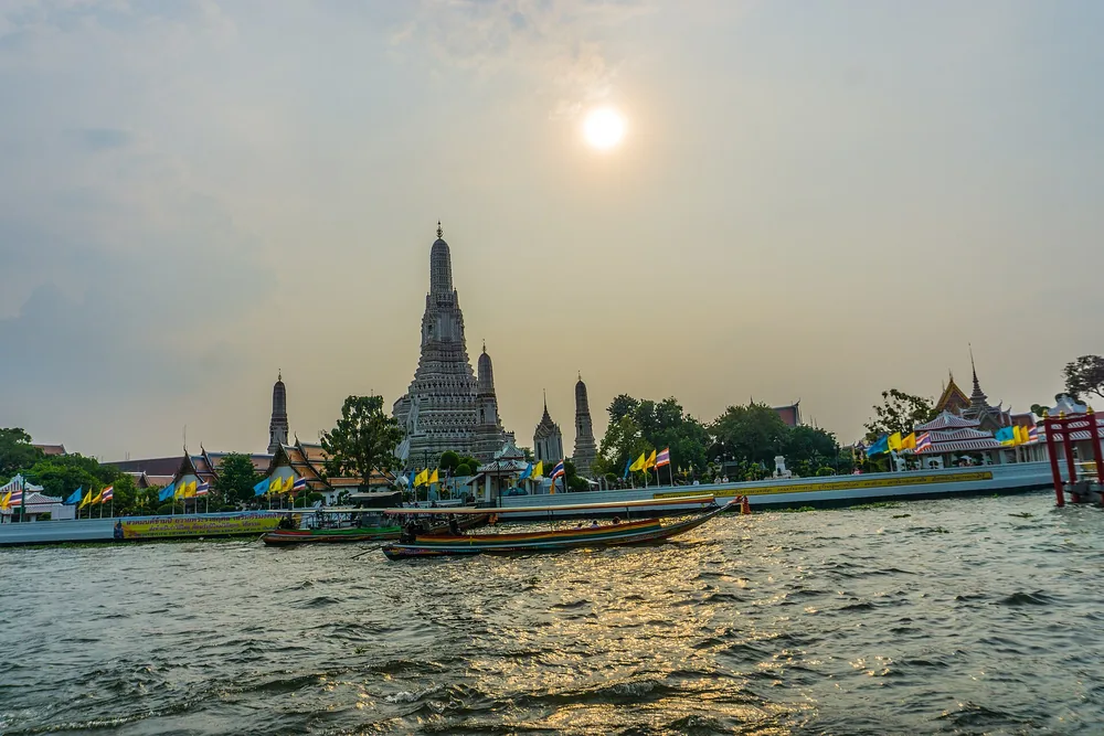 Wat Arun temple beside the Chao Phraya River at sunset in Bangkok. Destination context photograph.