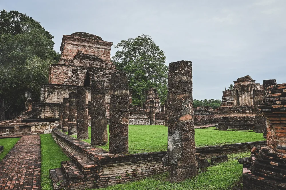 Brick temple ruins and stone columns at Wat Mahathat in Sukhothai Historical Park. Destination context photograph.