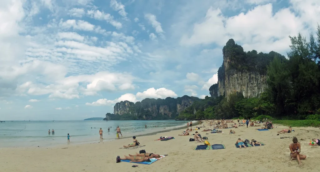 Limestone cliffs curve around turquoise water and white sand at Railay Beach in Krabi.